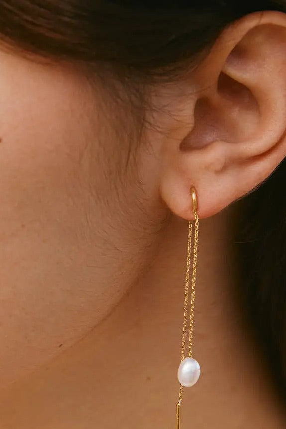 Gold earring with a pearl drop worn by a person