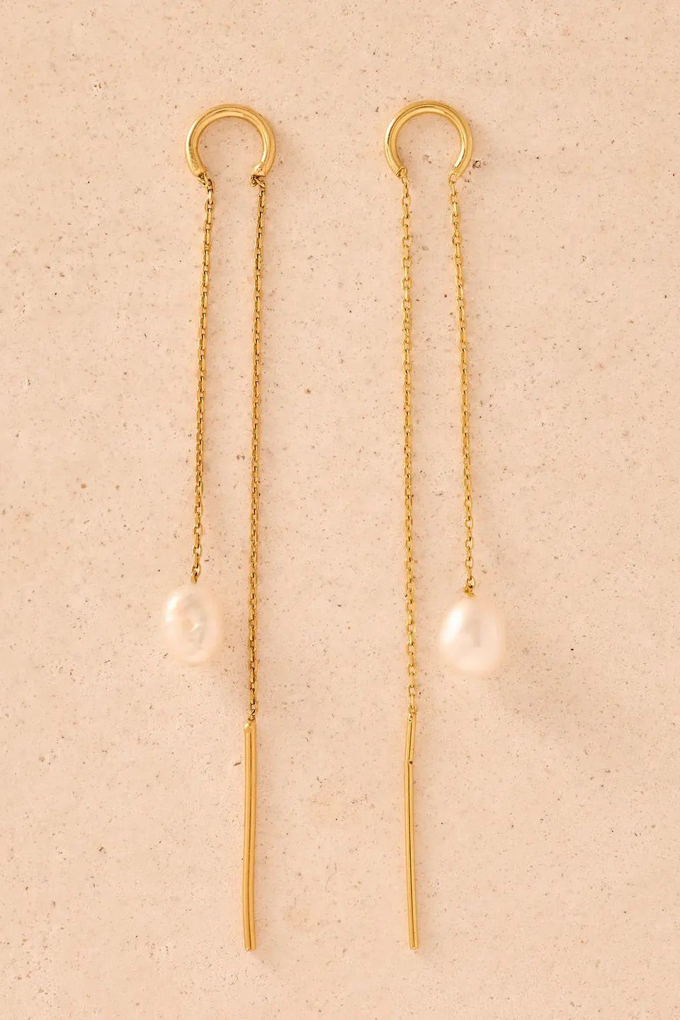 Gold chain earrings with pearl drops on a beige background