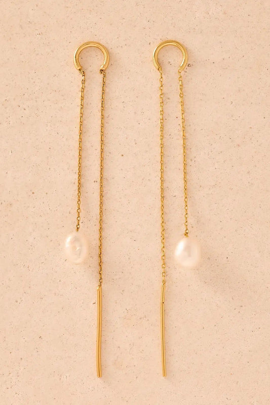 Gold chain earrings with pearl drops on a beige background
